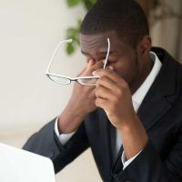 Man rubbing eyes while looking at computer Man rubbing eyes while looking at computer